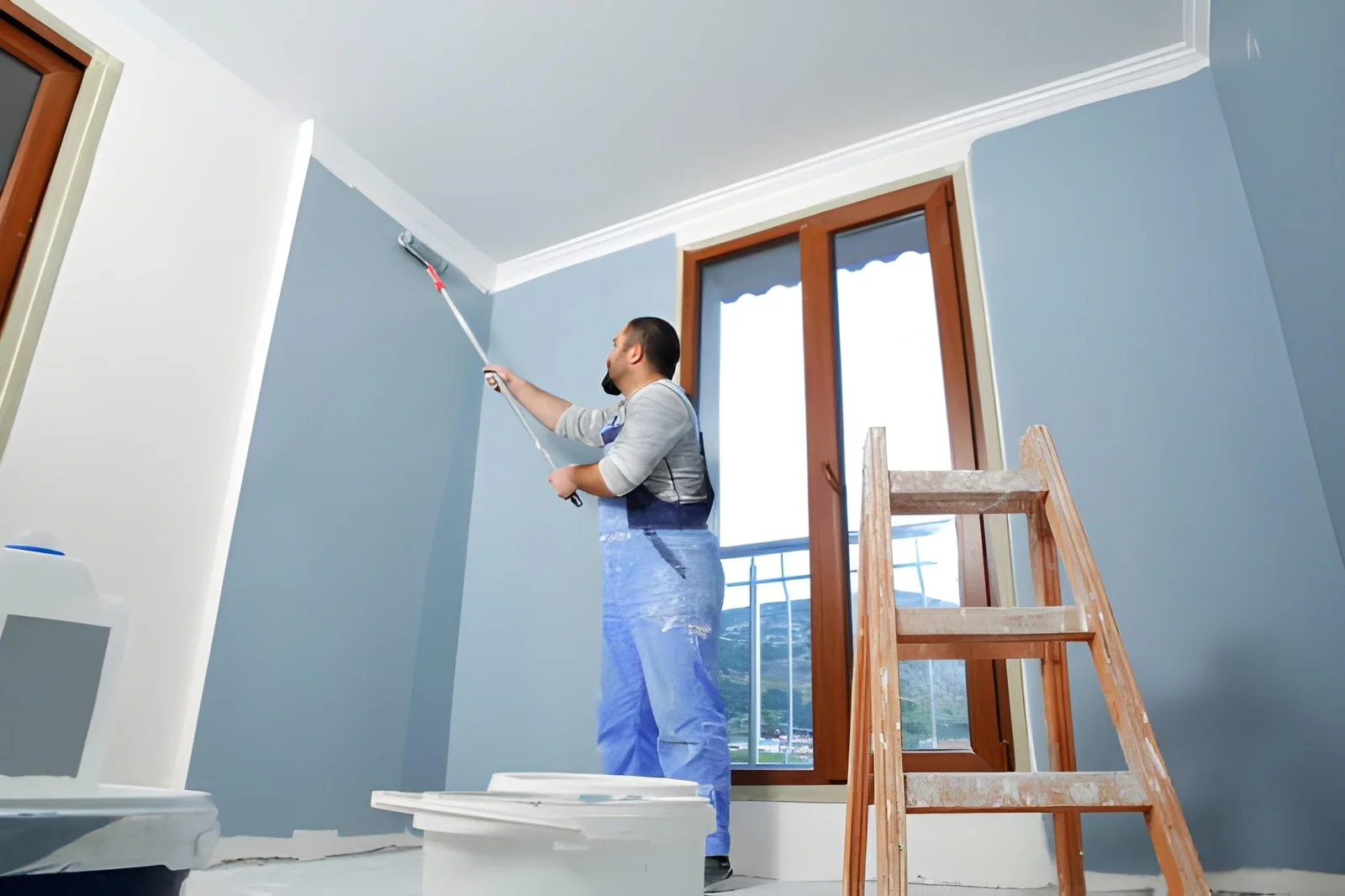 Painter rolling fresh paint onto a ceiling edge in a light blue interior room